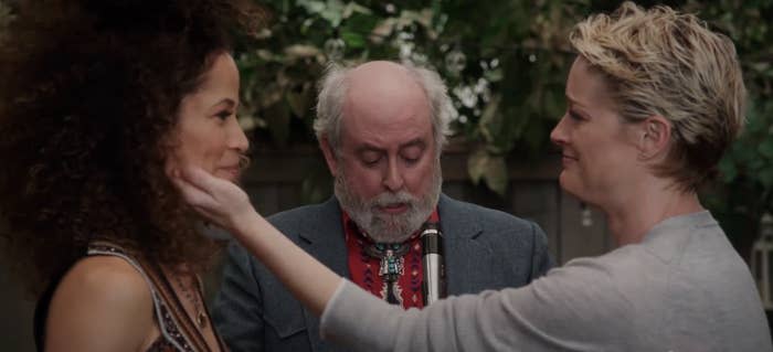 Sherri Saum and Teri Polo smile supportively at each other as a man officiates their wedding ceremony outdoors