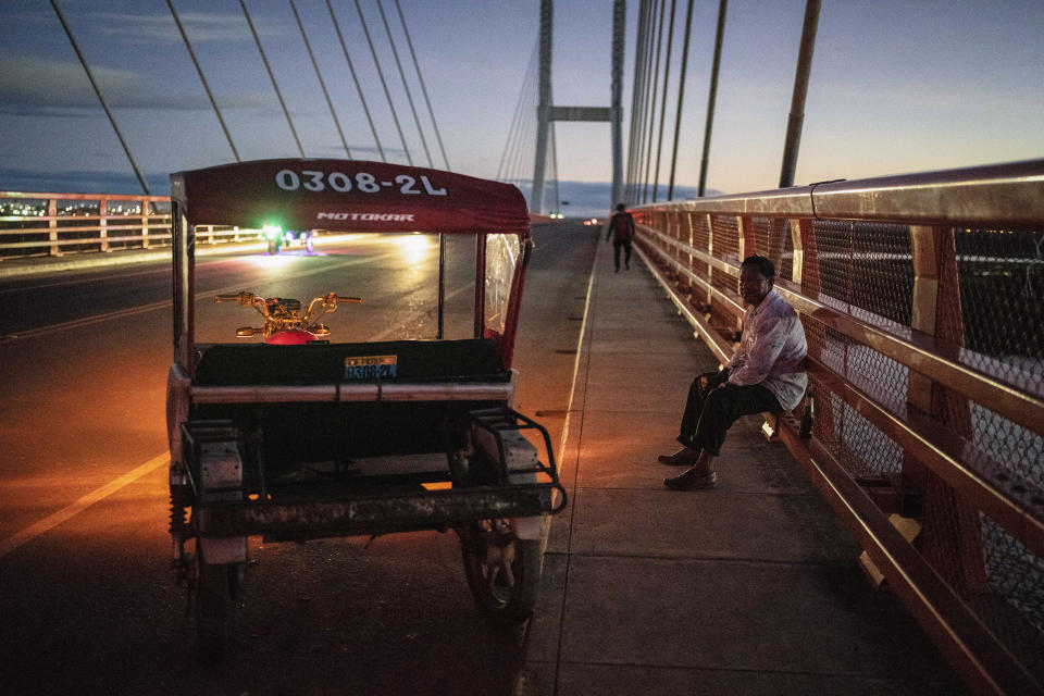 A moto-taxi driver rests on the railing of a federal highway bridge that extends over the Nanay River, in Iquitos, Peru, Monday, May 27, 2024. The project, which spans 188 kilometers (117 miles), is intended to connect Iquitos, the main city in Peru's Amazon, with the El Estrecho district on the Colombian border. (AP Photo/Rodrigo Abd)