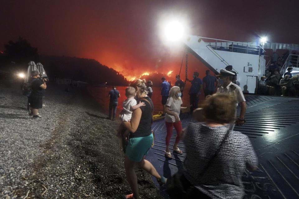 People embark a ferry during an evacuation from Kochyli beach as wildfire approaches near Limni village on the island of Evia, about 160 kilometers (100 miles) north of Athens, Greece, Friday, Aug. 6, 2021. Thousands of people fled wildfires burning out of control in Greece and Turkey on Friday, including a major blaze just north of the Greek capital of Athens that claimed one life, as a protracted heat wave left forests tinder-dry and flames threatened populated areas and electricity installations. (AP Photo/Thodoris Nikolaou)