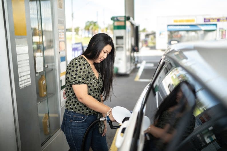 A woman fills up her car at a gas station.