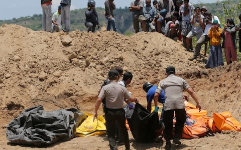 Rescue teams carry bodies to a mass grave in Palu - Credit: Tatan Syuflana/AP