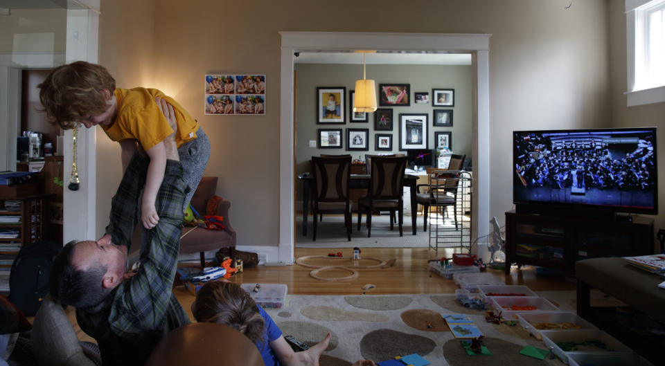 U.S. Army Field Band member Sgt. Major Robert McIver, Jr., is seen though an open window as he plays with is son Ethan, 4, in their Catonsville, Md., home, Thursday, March 26, 2020. The family is staying home because of the coronavirus outbreak. Inside on the television the U.S. Army Field Band's daily "We Stand Ready" virtual concert series from Fort George G. Meade is playing. The Army Field Band's mission is to bring the military's story to the American people. And they're not letting the coronavirus get in the way. (AP Photo/Carolyn Kaster)