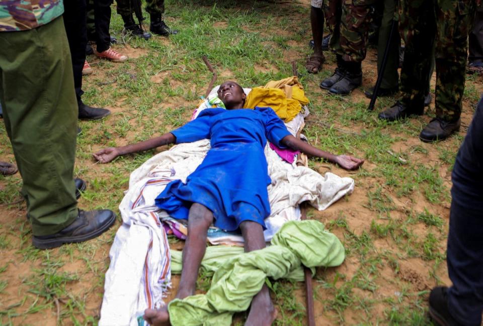 An emaciated member of a Christian cult named as Good News International Church, whose members believed they would go to heaven if they starved themselves to death, is guarded by Kenya police officers and officials from the civil society in Shakahola forest on 23 April (REUTERS)