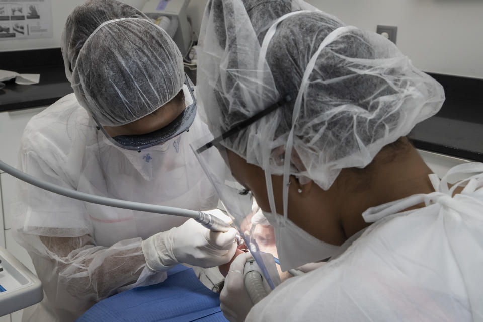 In this Wednesday, May 13, 2020 photo, dentist Sabrine Jendoubi, left, and her dental assistant Margot Daussat inspect the teeth of patient Veronique Guillot, during a dental appointment at a dental office in Paris. Those with toothache that suffered through France's two-month lockdown, finally have hope to end the pain. Dental practices are cautiously re-opening and non-emergency dentist appointments are now permitted around the country, as the French government eased confinement restrictions from Monday. (AP Photo/Michel Euler)