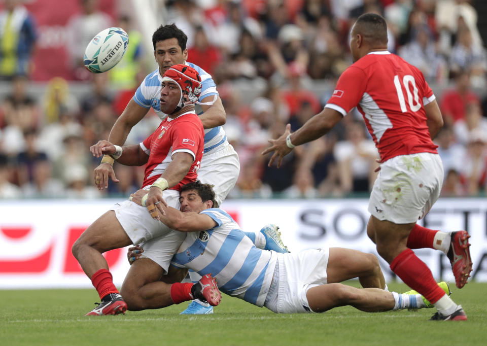 Tonga's Siale Piutau passes the ball to teammate James Faiva, right, as he is tackled by Argentina's Tomás Cubelli during the Rugby World Cup Pool C game at Hanazono Rugby Stadium between Tonga and Argentina in Osaka, Japan, Saturday, Sept. 28, 2019. (AP Photo/Aaron Favila)