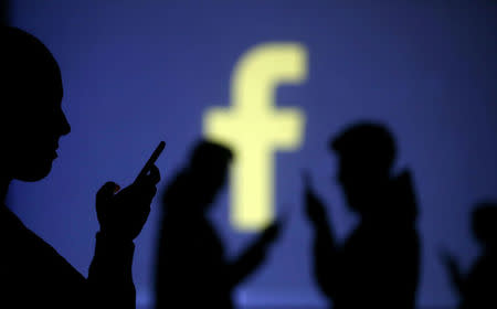 Silhouettes of mobile users are seen next to a screen projection of Facebook logo in this picture illustration taken March 28, 2018. REUTERS/Dado Ruvic/Illustration