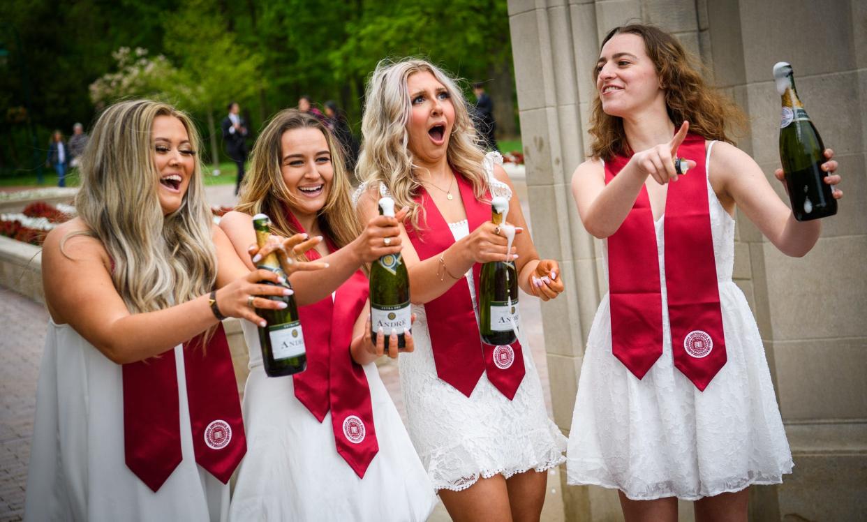 Indiana University graduating seniors, from left, Hannah Kerwin, Madison McGovern, Lexi Huchko and Bri Kramer laugh and react as they open a champagne bottle in front of the Sample Gates as they pose for graduation pictures on Thursday, May 5, 2022.