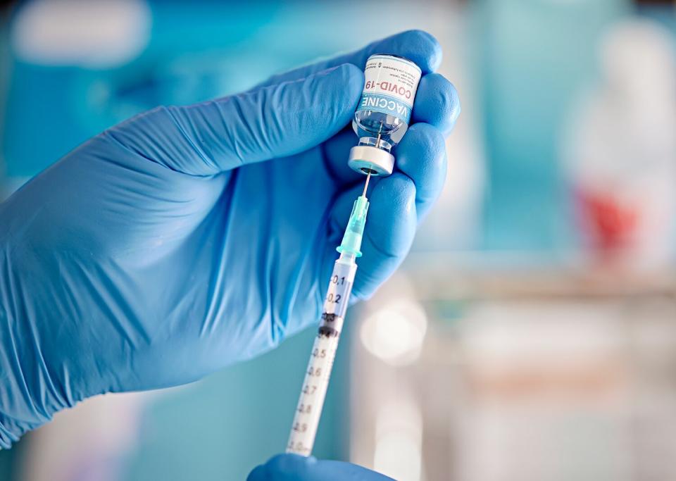 A healthcare Worker hands in surgical gloves pulling COVID-19 vaccine liquid from vial to vaccinate a patient