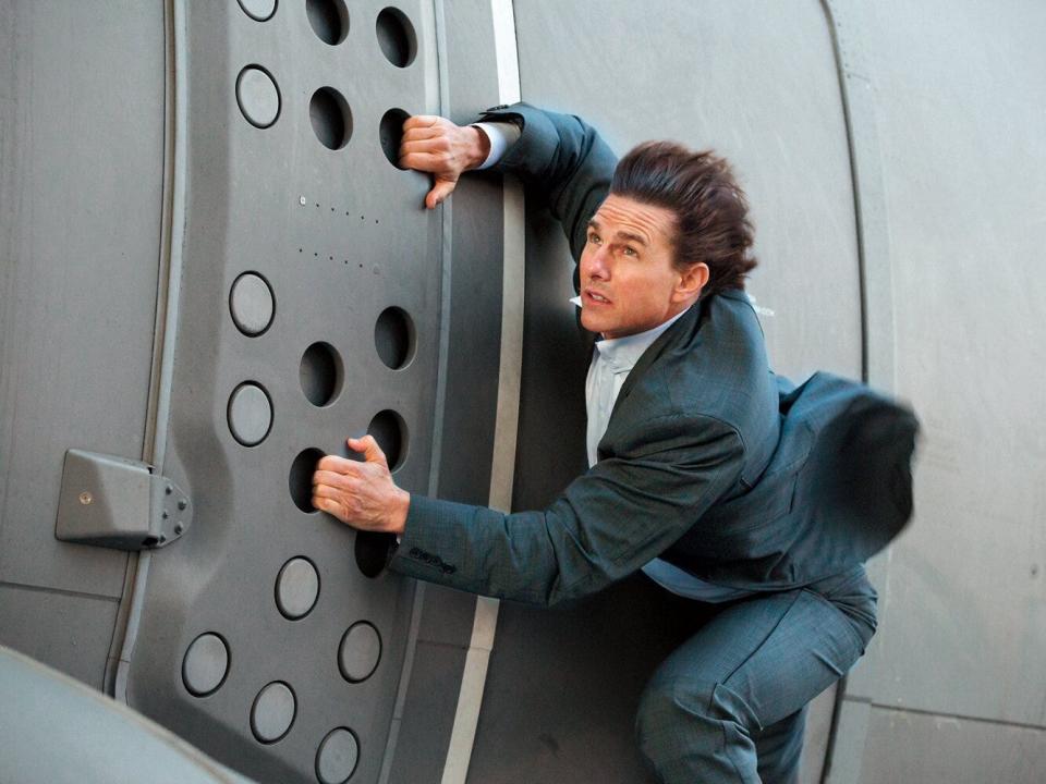 Tom Cruise in "Mission: Impossible - Rogue Nation" holding on to side of plane