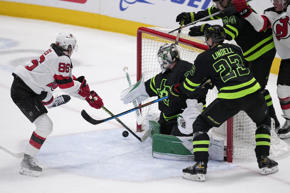 New Jersey Devils center Jack Hughes (86) takes a shot as Dallas Stars' Jake Oettinger, center, gets help defending on the play from Esa Lindell (23) in the first period of an NHL hockey game, Friday, Jan. 27, 2023, in Dallas. (AP Photo/Tony Gutierrez)