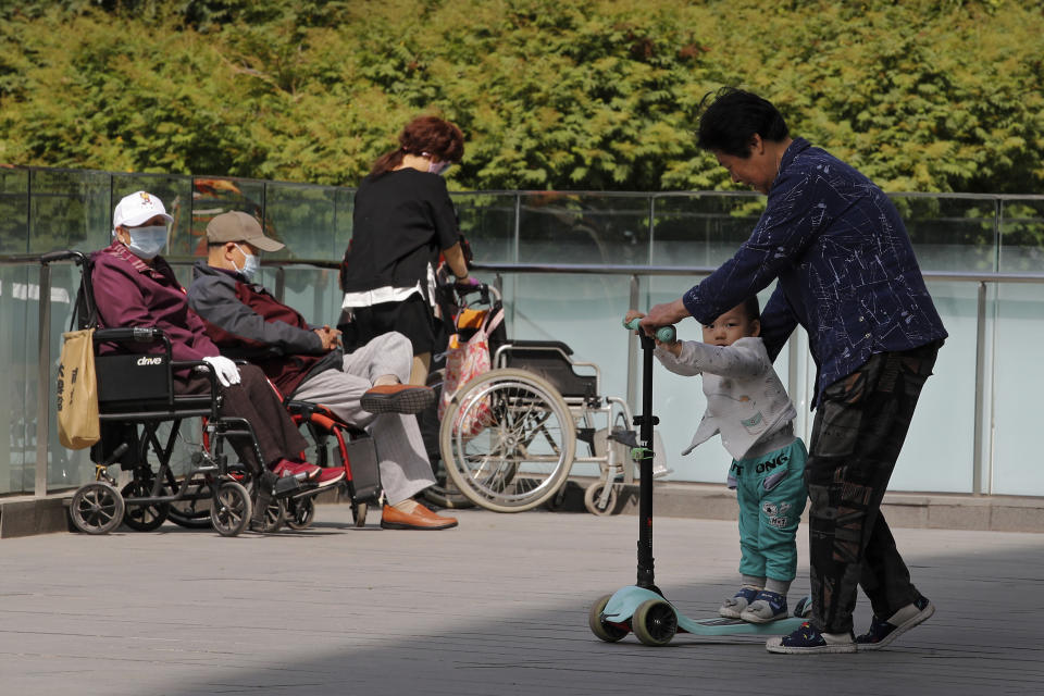 A woman plays with a child near elderly people on wheelchairs sunbathing on a compound of a commercial office building in Beijing on Monday, May 10, 2021. China’s population growth is falling closer to zero as fewer couples have children, the government announced Tuesday, May 11, 2021, adding to strains on an aging society with a shrinking workforce. (AP Photo/Andy Wong)