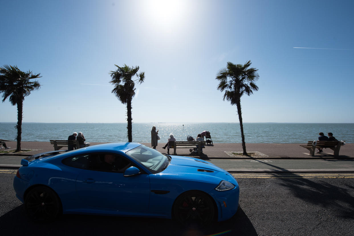 SOUTHEND, ENGLAND - MARCH 29: People sit on benches to enjoy the warm weather as a Jaguar XKR-S sports car passes by on the promenade beside the beach in the warm weather on March 29, 2021 in Southend, England. Today the government eased its rules restricting outdoor socialising and sport in England, the first milestone on the government's 