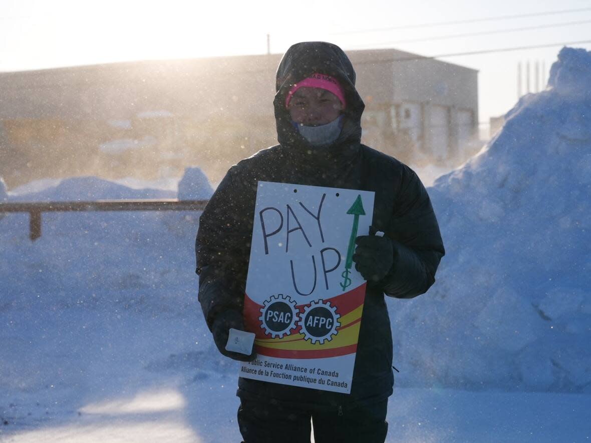 A striking Iqaluit Housing Authority worker stands outside the housing authority on a frigid Friday morning. Picketing began at about 8 a.m. last Friday. (Alicia Lee/CBC - image credit)