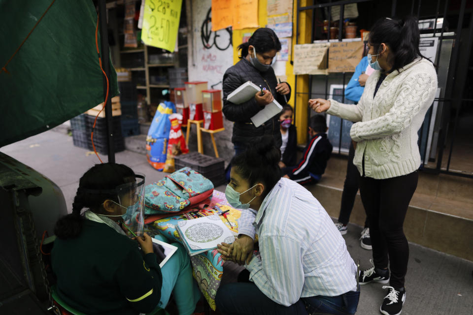 Dalia Davila Neri, who runs "Tortillerias La Abuela," or "Granda's Tortilla Shop with her husband, assists student Aide Joselin Hernandez Moreno while she learns on a donated tablet outside Davila's shop on the southern edge of Mexico City, Friday, Sept. 4, 2020. Concerned about the educational difficulties facing school-age children during the coronavirus pandemic, Davila and her husband adapted several spaces outside their locale to provide instruction and digital access to locale children who don't have internet or TV service at home, a project which has attracted donations and a waiting list of students. (AP Photo/Rebecca Blackwell)