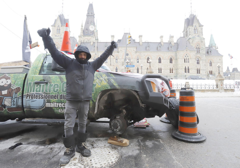 A man who removed the tires from his pickup truck stands in front of West Block on Parliament Hill as a rally against COVID-19 restrictions, which began as a cross-country convoy protesting a federal vaccine mandate for truckers, continues in Ottawa, Canada, Monday, Jan. 31, 2022. (Patrick Doyle/The Canadian Press via AP)