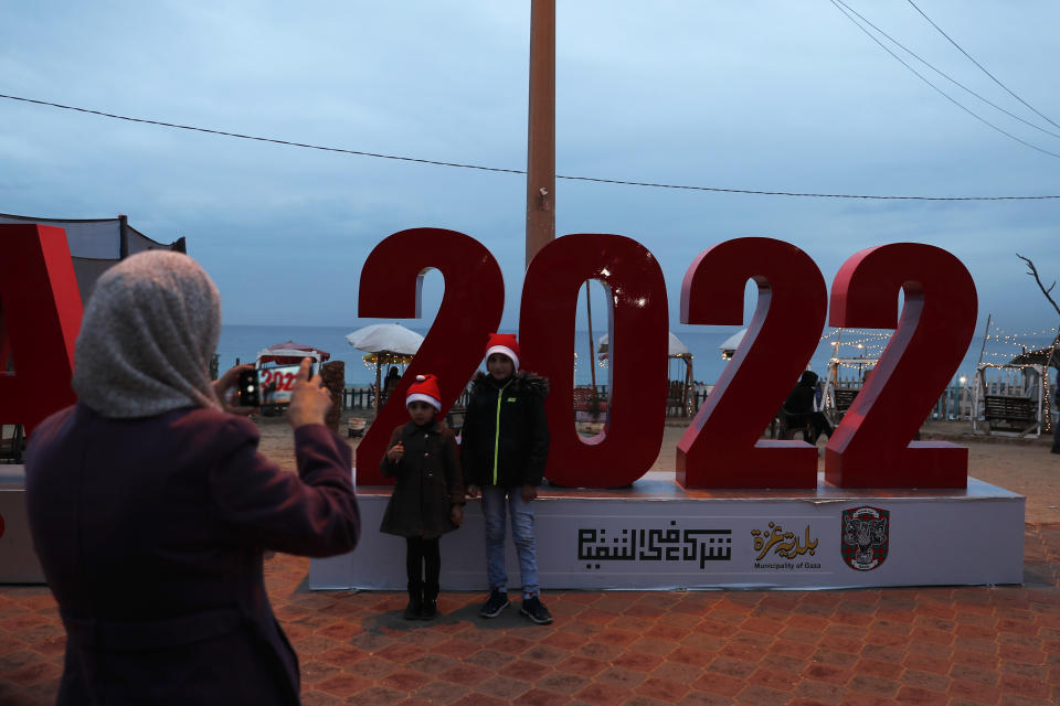 A Palestinian woman takes photos of her children near the beach on the last day of the year and New Year's celebrations, in Gaza City, Friday, Dec. 31, 2021. (AP Photo/Adel Hana)