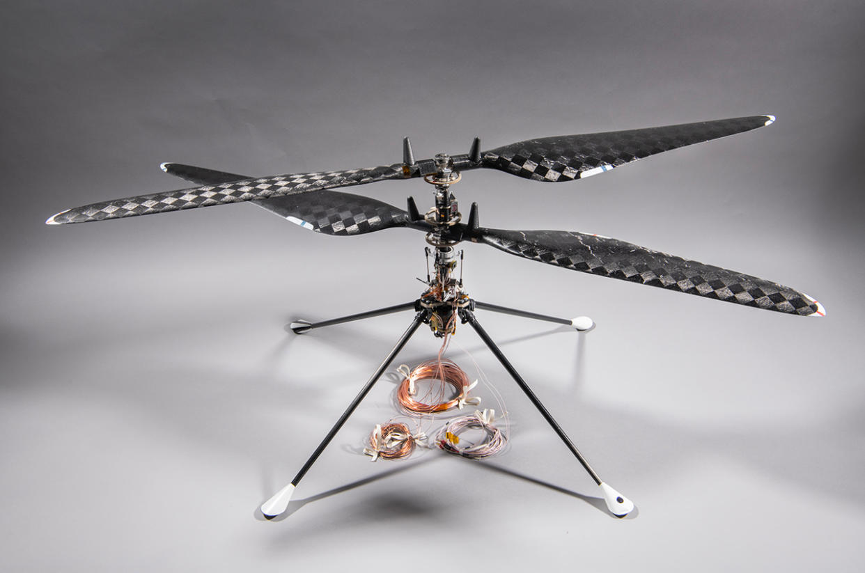  A small, four-rotor drone sits on a grayish-white surface. 