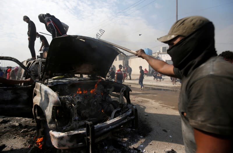 Protesters step on a military vehicle of Iraqi security forces after burning it, during ongoing anti-government protests in Basra