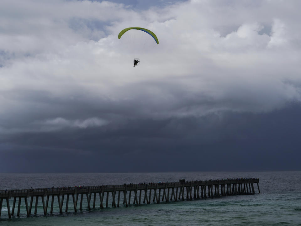 A paraglider flies over Navarre Beach Fishing Pier as storm clouds approach the shore in Navarre Beach, Fla., Sunday, June 16, 2024. (AP Photo/Kiichiro Sato)