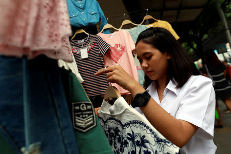 A university student holds clothes as she helps her parents who are street vendors in a street in Bangkok, Thailand, September 12, 2018. Picture taken September 12, 2018. REUTERS/Soe Zeya Tun