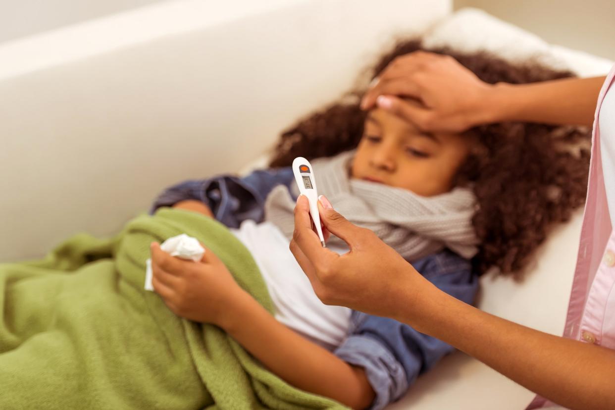 Little African America girl sick on the couch getting her temperature taken