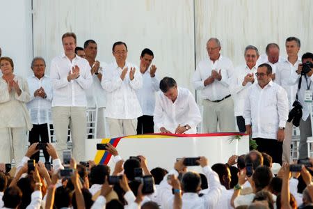 Colombian President Juan Manuel Santos (C) signs an accord ending a half-century war that killed a quarter of a million people, as Marxist rebel leader Rodrigo Londono (front, R), known by his nom de guerre Timochenko, looks on in Cartagena, Colombia, September 26, 2016. REUTERS/John Vizcaino
