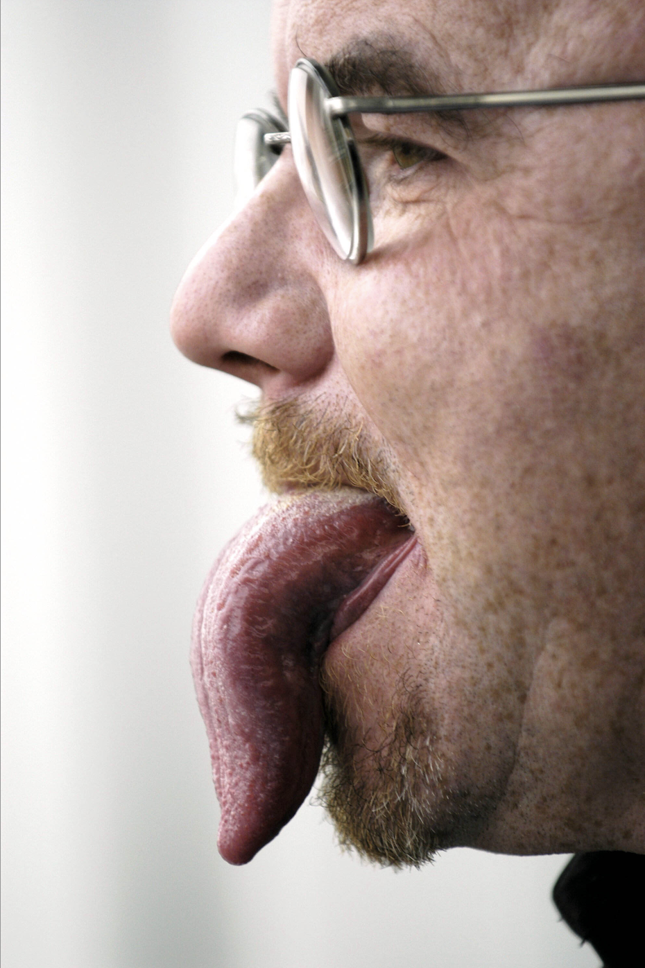 Close-up of a man's tongue sticking out and down to the bottom of his slightly bearded chin