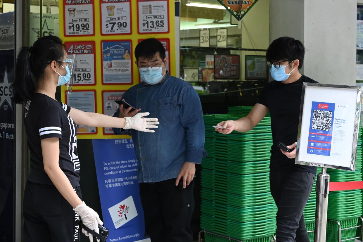 A man preparing to enter a supermarket presents his identity document to a staff member for verification before entering its premises, as a preventive measure against the spread of the COVID-19 novel coronavirus, in Singapore on May 2, 2020. (Photo by Roslan RAHMAN / AFP) (Photo by ROSLAN RAHMAN/AFP via Getty Images)