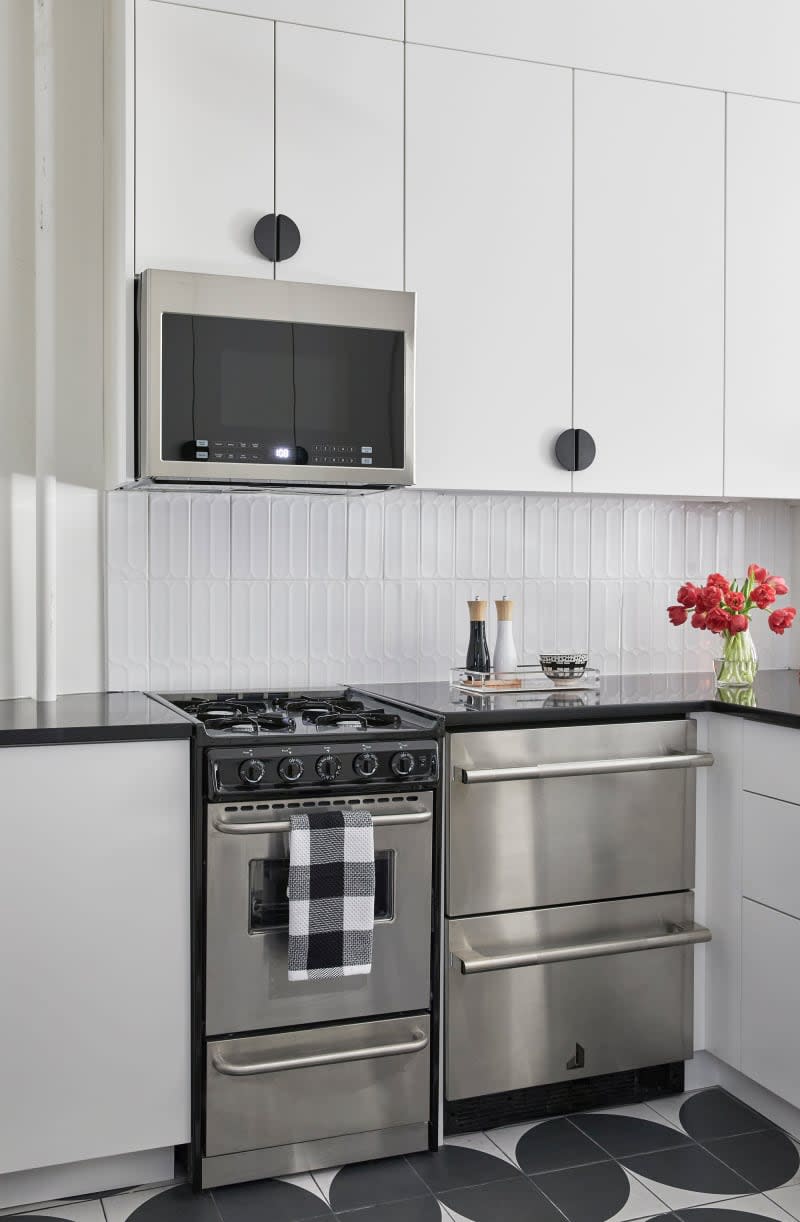 Updated kitchen with stainless steel appliances and white cabinets with large black pulls after renovation.