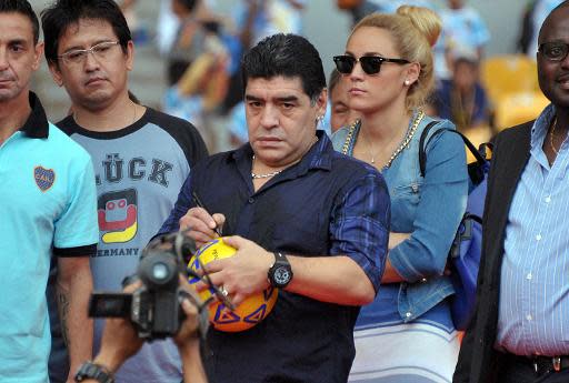 El exastro del fútbol argentino Diego Maradona (C) firma un balón antes de patearlo a fans presentes durante una clínica de entrenamiento en el estadio Bung Karno, en Jakarta, el 29 de junio de 2013. (AFP | Bay Ismoyo)