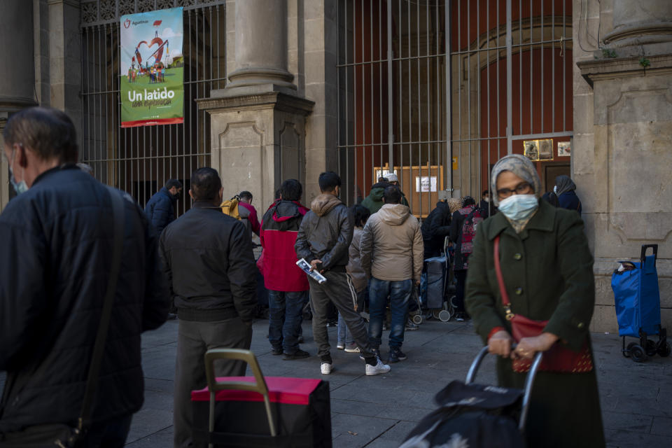 People wait their turn to receive a weekly pack of donated food and supplies, outside a church in Barcelona, Spain, Wednesday, Feb. 3, 2021. Food requests have increased considerably in the last months as Spain has been in lockdown to fight the coronavirus pandemic. (AP Photo/Emilio Morenatti)