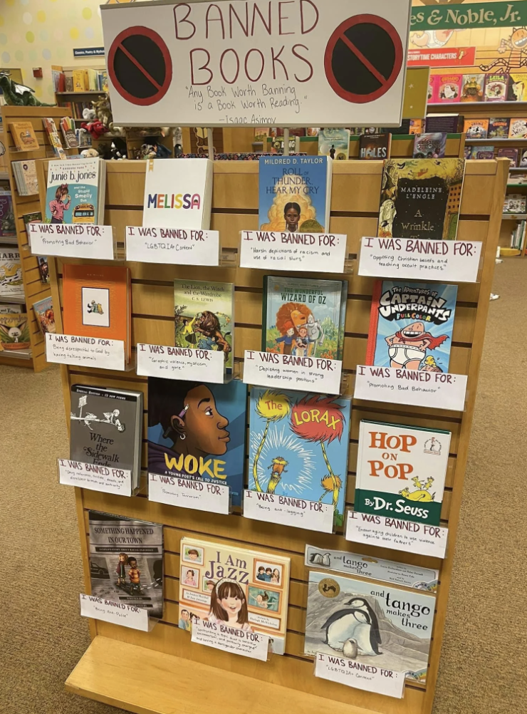 Books display with a sign "Banned Books: Any Book Worth Banning is a Book Worth Reading." It includes titles like "Melissa," "Woke," and "I Am Jazz" with reasons for banning