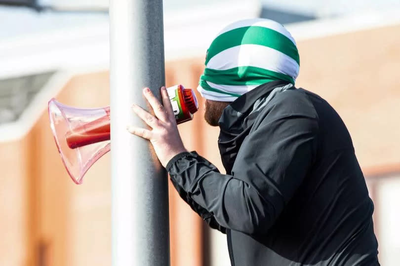 A Celtic ultra masked in a balaclava leads the crowd into song.