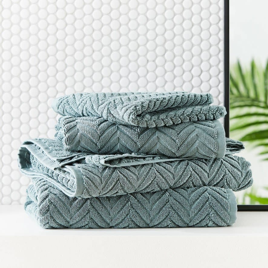 A set of green textured towels in a white bathroom 