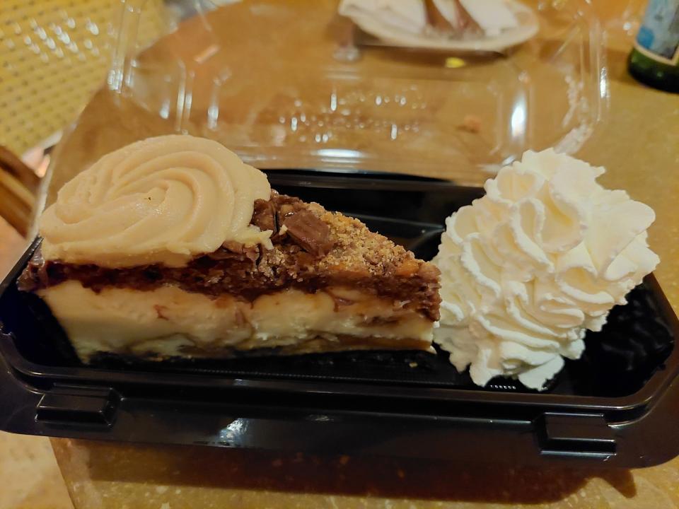 A photo of a slice of the Adam's Peanut Butter Cup Fudge Ripple Cheesecake in a tray at the Cheesecake Factory