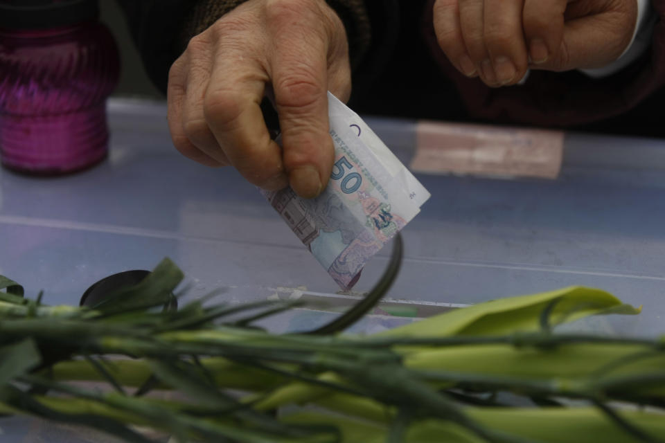 A man puts a 50 hryvnias banknote inside a box as part of a donation for the people still camped out on Kiev's Independence Square, the epicenter of the country's current unrest, Ukraine, Tuesday, Feb. 25, 2014. Ukraine needs money, and fast _ in weeks, not months. But bailing out the country of 46 million people will not be as easy as simply writing a big check. For one, Ukraine has already burned the main international financial rescuer, the International Monetary Fund, by failing to keep to the terms of earlier bailouts from 2008 and 2010. Now it needs help again, and its economic and financial problems are worse than before. (AP Photo/Marko Drobnjakovic)