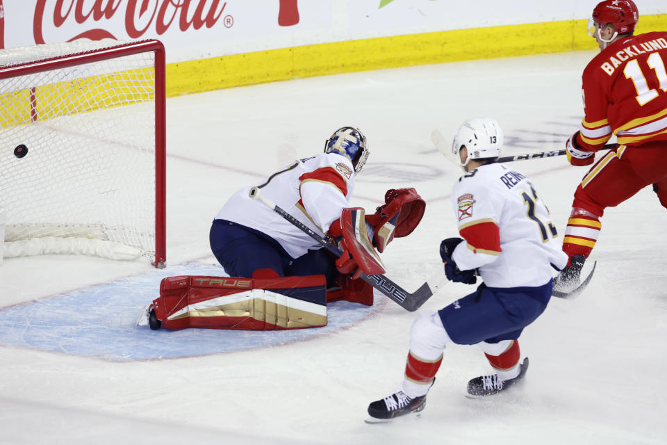 Calgary Flames center Mikael Backlund, right, scores a short-handed game-winning goal against Florida Panthers goalie Anthony Stolarz, left, as Florida center Sam Reinhart looks on during the third period of an NHL hockey game in Calgary, Alberta, Monday, Dec. 18, 2023. (Larry MacDougal/The Canadian Press via AP)