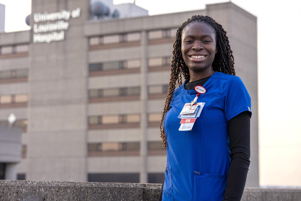 In this Feb. 1, 2022, photo provided by University of Louisville Hospital, Faith Akinmade, an ICU nurse at the University of Louisville Hospital in Louisville, Ky., who is originally from Nigeria, poses for a photo in front of the hospital. After completing college in the United States, Akinmade has been working at the hospital, but her work permit is set to expire in March and she said she needs it renewed, or her green card approved, to stay on the job. Hospitals and recruiters are hoping international nurses like Akimnade and others overseas will be able to snap up a larger-than-usual number of immigrant visas that are available this fiscal year to professionals seeking to move to the United States. (Tom Round/University of Louisville Hospital via AP)