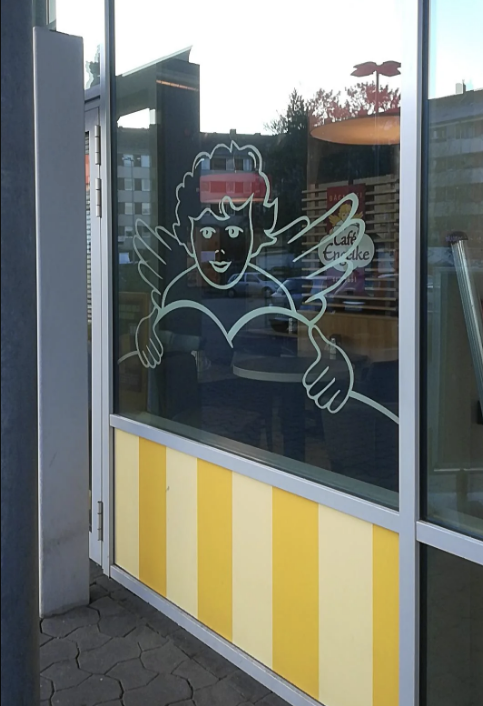 Storefront with large glass windows featuring an illustration of an angel holding a book, with the text "Café Engelke" visible in the reflection