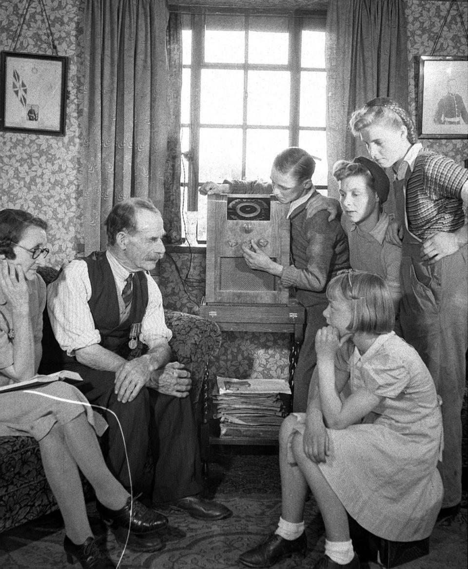<p>A family gathers around the wireless to listen to the celebration from afar.</p>
