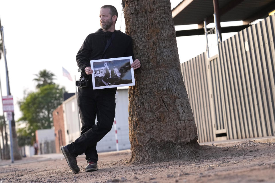 Documentary photographer Eric Elmore displays one of his images of Roosevelt White III while standing on the location where Roosevelt's tent use to be, Tuesday, Dec 19, 2023, in Phoenix. Elmore documented Phoenix's homeless people in addition to Roosevelt, who was 36 when he died of a stroke in September after falling ill in the Phoenix homeless encampment known as "The Zone". Roosevelt is among thousands of homeless people who died this year and are being remembered at winter solstice events for Homeless Persons' Memorial Day. (AP Photo/Matt York)