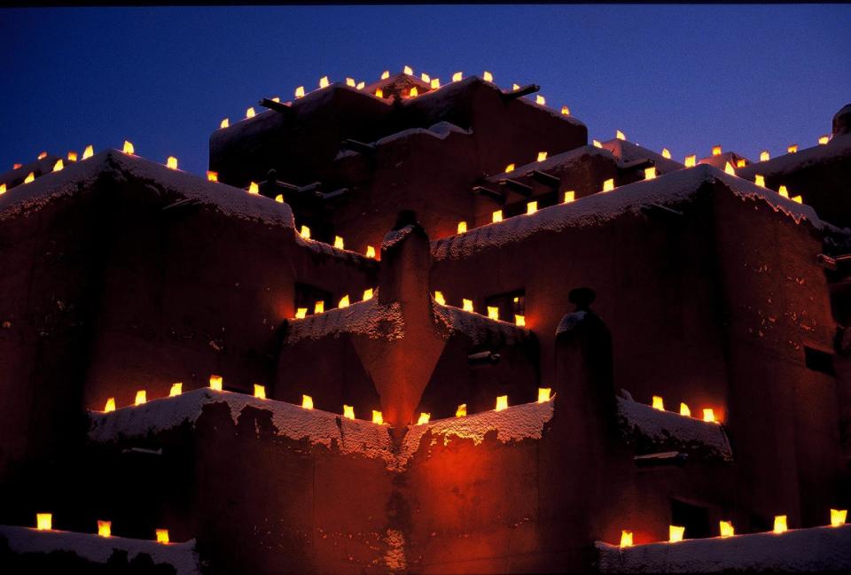 This undated image provided by New Mexico Tourism shows farolitos, which are candles in paper bags, flickering against the night sky atop Santa Fe’s Inn at Loretto. The farolito lanterns, also called luminarias, are a New Mexico holiday tradition. (AP Photo/New Mexico Tourism Department)