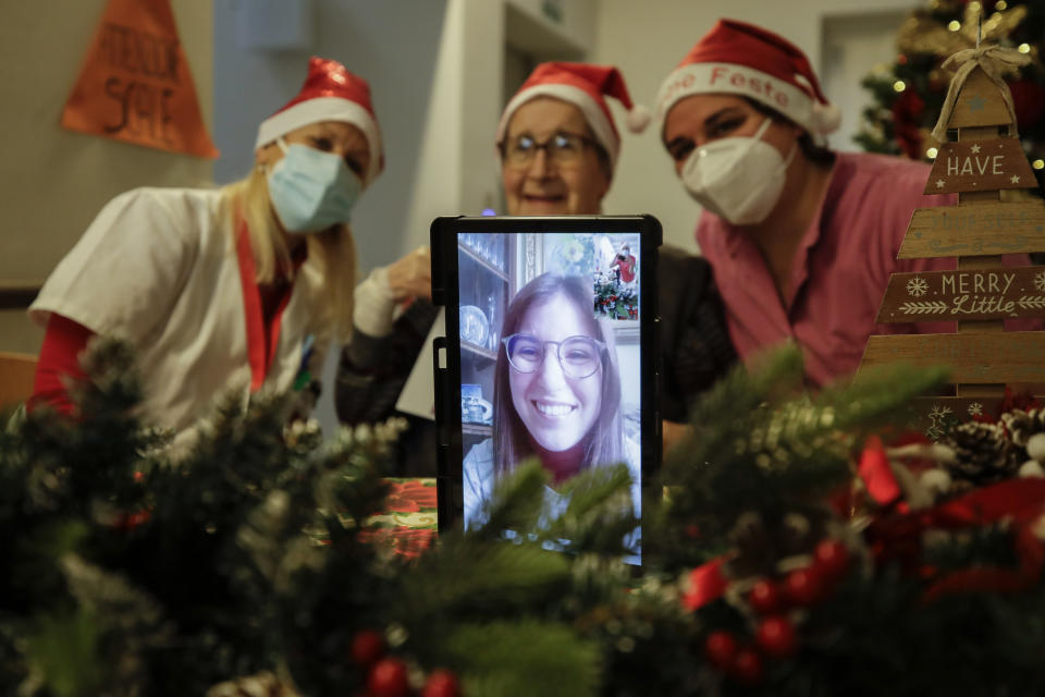 Carolina Previtali, 93, center, is flanked by director Maria Giulia Madaschi, left, and carer Melania Cavalieri as she talks on a video call with Eleonora Nola, a donor unrelated to her, who bought and sent her a Christmas present through an organization dubbed "Santa's Grandchildren", at the Martino Zanchi nursing home in Alzano Lombardo, one of the area that most suffered the first wave of COVID-19, in northern Italy, Saturday, Dec. 19, 2020. (AP Photo/Luca Bruno)