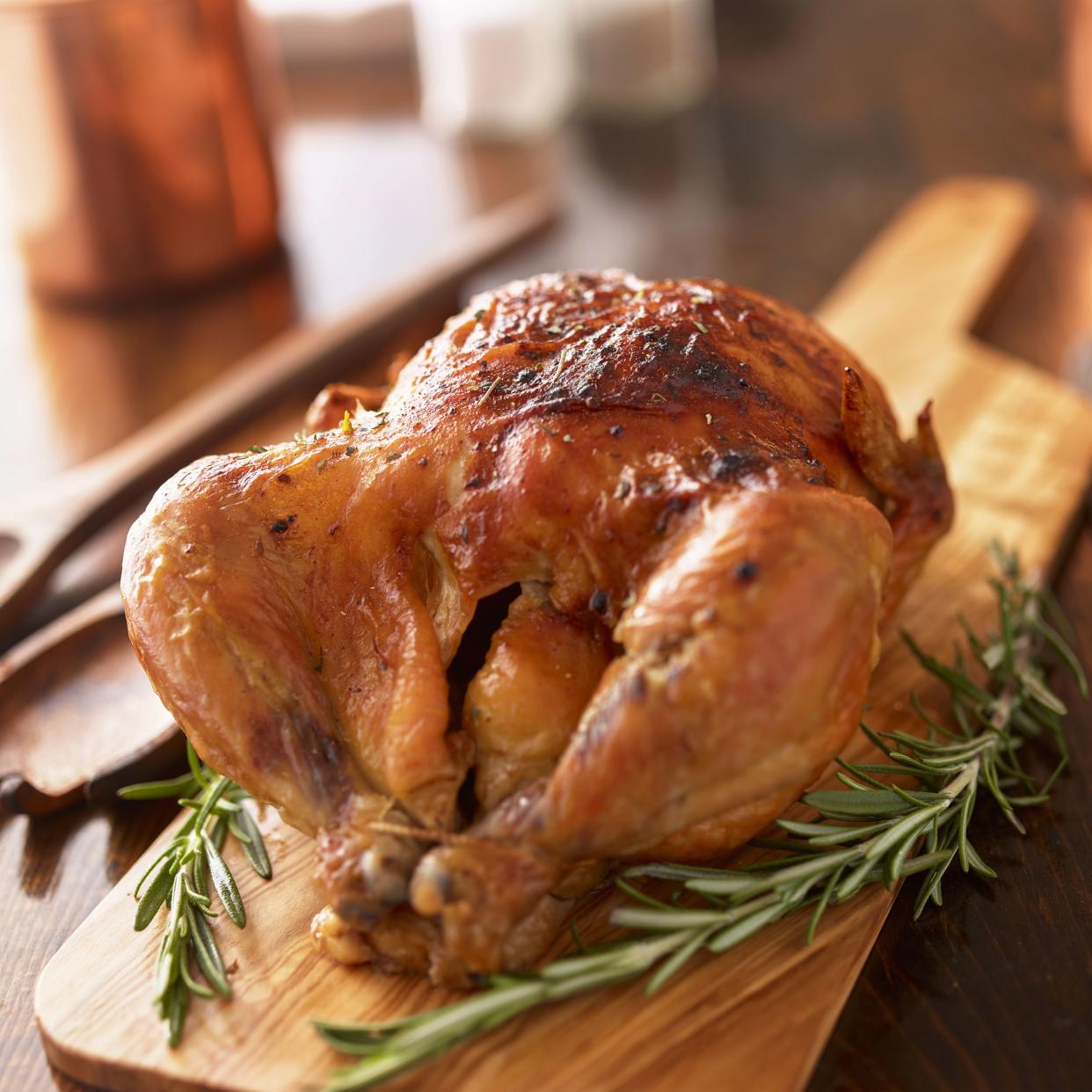 Rotisserie chicken on wooden serving tray with two sprigs of rosemary.