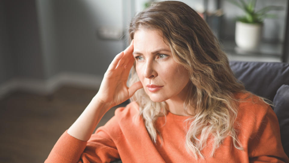 A woman in an orange shirt holding her hand to her temple with either a migraine vs tension headache