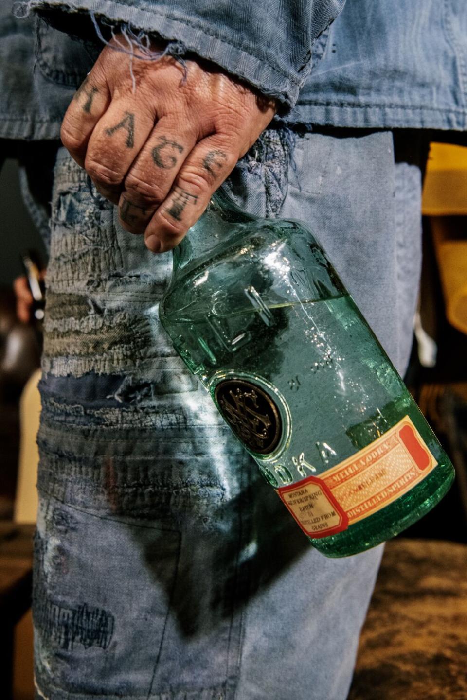 A man's tattooed hand holding a bottle of vodka