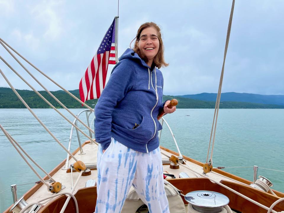 A woman standing at the front of a boat in a sweatshirt on a lake.