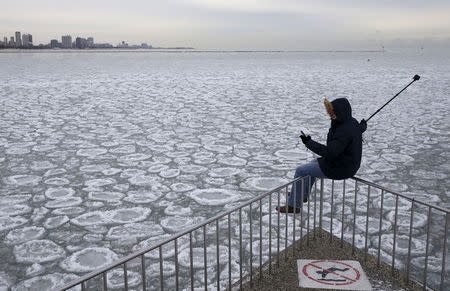 A man sits on a railing to take a 'selfie' picture, overlooking the partially frozen Lake Michigan in Chicago, Illinois, in this January 5, 2015 file photo. REUTERS/Jim Young/Files