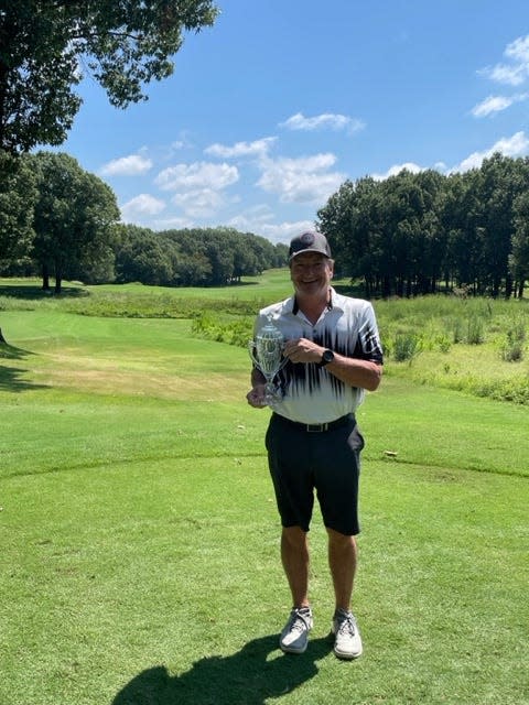 A man in a white shirt an black cap on a golf course carrying a silver trophy