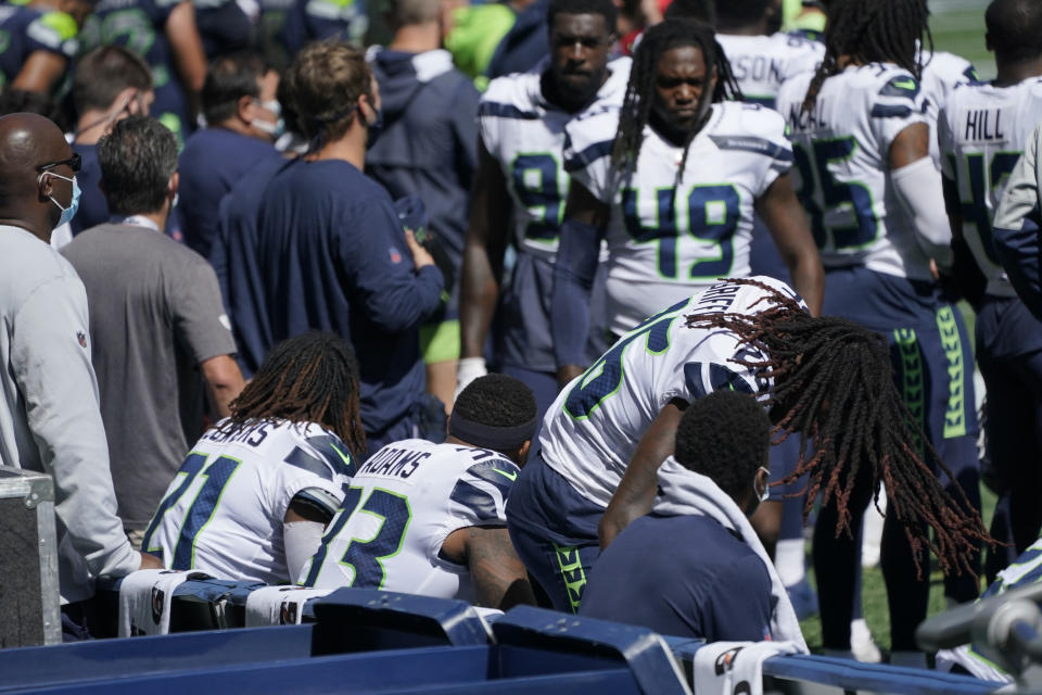 Seattle Seahawks cornerback Shaquill Griffin, lower right, flips his hair as he sits down on the bench during the singing of the national anthem before an NFL football mock game, Wednesday, Aug. 26, 2020, in Seattle. Griffin was joined by other players, including his brother, linebacker Shaquem Griffin (49) in sitting during the anthem. (AP Photo/Ted S. Warren)